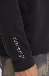Felpa nera in pile con una texture morbida e un logo sulla manica che legge "POLARTEC" in bianco. Il design è semplice e funzionale.