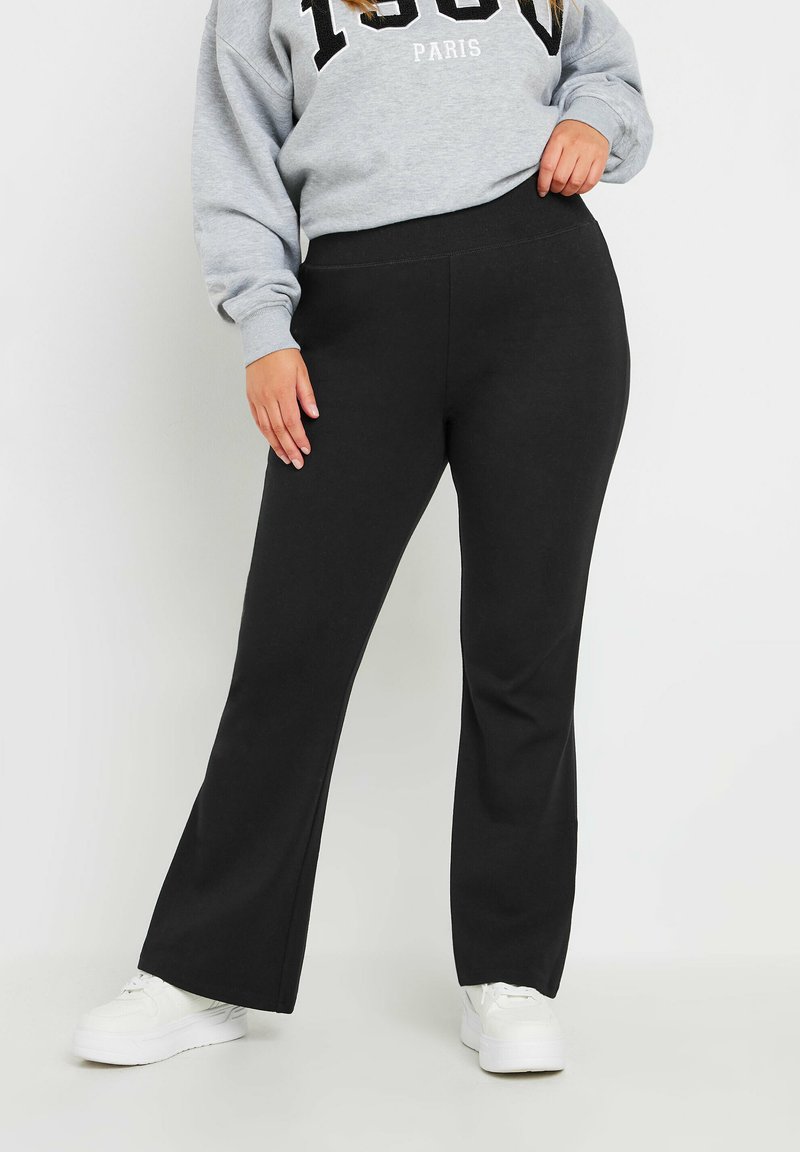 Musta leveälahkeinen housu pehmeästä kankaasta, jossa on joustava vyötärö mukavuutta varten. Yhdistetty harmaaseen huppariin ja valkoisiin tennareihin.