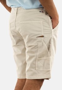 Shorts cargo beiges avec plusieurs poches, en tissu léger. Présentent une fermeture éclair et des coutures décoratives sur les côtés.