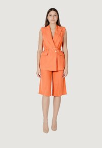 Completo in lino arancione composto da blaser senza maniche con cintura e tasche e pantaloni corti a gamba larga. Tessuto morbido, vestibilità su misura.