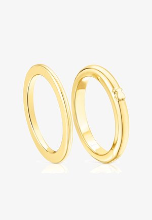 Pierścienie w kolorze złotym o gładkiej, polerowanej powierzchni. Jeden z nich ma delikatne wcięcie jako detal, oba mają owalny kształt.