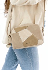 Beige axelremsväska med geometrisk lapptäckedesign, med suedes och lädertexturer, justerbar rem och metallogotyp.