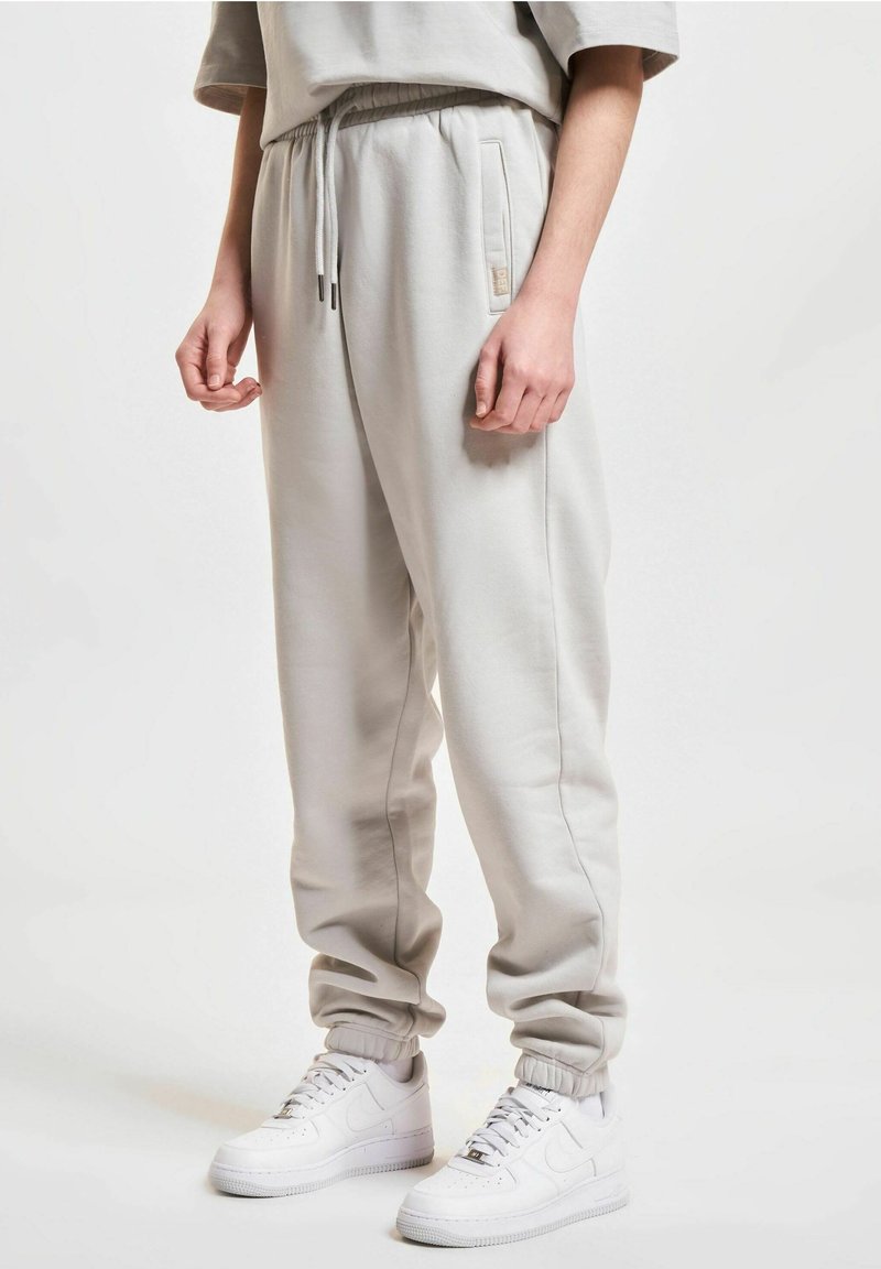 Light gray sweatpants with an elastic waistband, side pockets, ribbed cuffs, and a soft texture, paired with white sneakers.