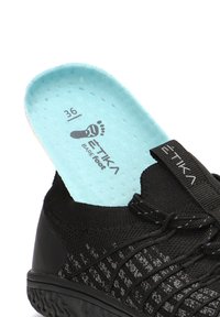 Zapatilla deportiva negra con una plantilla azul claro etiquetada "ETIKA BAREfoot" y la talla 36 visible en el interior.