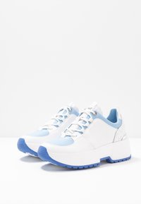 Vita sneakers med blå accenter och strukturerad sidor, med en tjock vit sula med blå slitbanor och snörningsdesign.