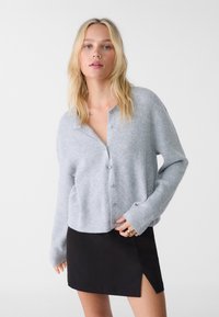 Cardigan grigio a coste con bottoni sul davanti, vestibilità rilassata e maniche lunghe, abbinato a una gonna mini nera con uno spacco laterale.