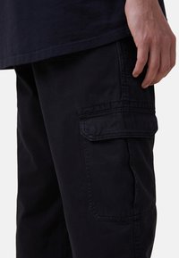 Mörkblå cargobyxor med texturerad tyg, sidofickor och synlig sömnad. Midjan är något avsmalnande för en figurnära look.