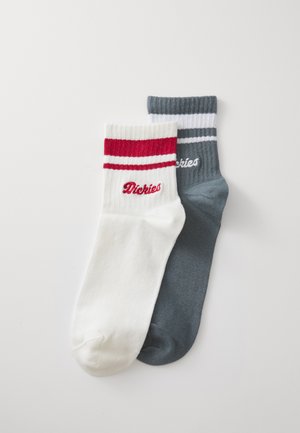 Puhvelista valmistetut miehustossut, yksi valkoinen punaisilla raidoilla ja logolla, yksi harmaa valkoisilla raidoilla ja logolla, näyttäen ribbikuvioita ja kontrastivärejä.