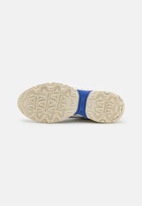 Semelle de sneaker gris clair avec une semelle extérieure en caoutchouc texturé, présentant un accent de semelle intermédiaire bleue et un motif de bande de roulement angulaire distinct.