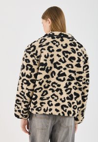 Kabát z umelej kožušiny s leopardím vzorom v béžovej a čiernej farbe, s golierom a voľným strihom. Textúrovaný povrch z mäkkej a huňatej tkaniny.