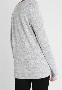 Maglia a maniche lunghe grigia mélange realizzata in morbido tessuto a maglia, con scollatura arrotondata e vestibilità comoda, abbinata a pantaloni neri.