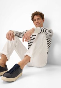 Marineblauwe lage sneakers met een gestructureerde leren bovenkant, witte rubberen zool en donkere veters, gecombineerd met een gestreepte trui en witte broek.