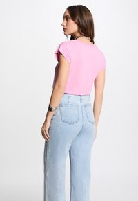 Maglietta rosa a maniche corte con un design aderente, abbinata a jeans azzurri a vita alta con un classico stile a cinque tasche.