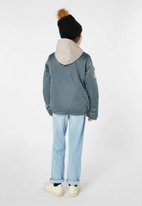 Hellblau bomberjacke mit einer grauen Kapuze, elastischen Bündchen und Taillengummi. Kombiniert mit geraden, hellen Jeans und weißen Turnschuhen. Schwarz gestrickte Mütze.