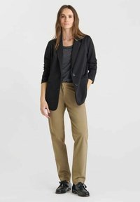 Blazer noir à deux boutons, sur une chemise rayée grise, associé à un pantalon beige et des chaussures noires à lacets. Design simple et ajusté.