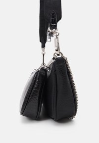 Dwie czarne torebki crossbody o teksturowanych powierzchniach i srebrnych akcentach, połączone metalowymi zapięciami i szerokim czarnym paskiem, wiszące obok siebie.