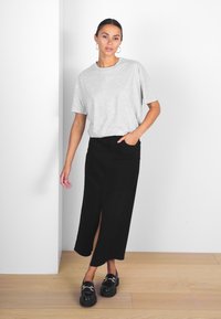 T-shirt gris à manches courtes avec une coupe décontractée, associé à une jupe noire longueur cheville avec une fente sur le côté, et des mocassins noirs.