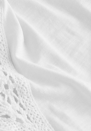 Biała tkanina z teksturowanym koronkowym detalem na jednej krawędzi, o gładkiej, miękkiej powierzchni i subtelnym połysku.