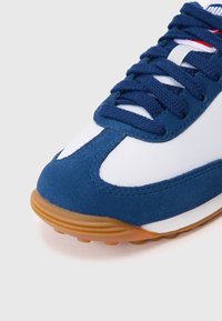 Kék velúr és fehér hálós sneaker, barna gumitalppal, tengerészkék fűzőkkel és piros kiegészítőkkel a nyelv közelében.