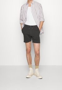 Shorts gris avec taille élastique et cordon de serrage, associés à une chemise à rayures beige clair et blanche à boutons. Baskets crème et chaussettes beiges.