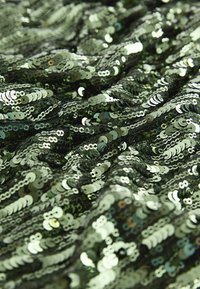 Tissu en sequins verts avec une texture ondulée, présentant des sequins circulaires superposés dans différentes nuances de vert, reflétant la lumière.