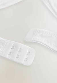 Hvide justerbare stropper lavet af blødt stof, med en kroklukning og tre spændere samt flade kanter for et sømløst design.