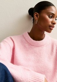 Różowy sweter dziergany z ribbowym dekoltem i mankietami, z miękkim, teksturowanym wykończeniem. Nosi się w casualowym, luźnym kroju.