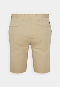 Shorts beige pour hommes, longueur genou, avec passants de ceinture et deux poches passepoilées arrière, vus de dos sur un fond uni.