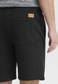 Des shorts en coton noirs présentent une poche arrière avec une étiquette discrète, une taille élastique et une texture lisse avec une coupe ajustée.