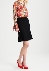 Blus med långa ärmar i röd och blommig mönster, tillsammans med en svart utsvängd kjol och röda högklackade skor med spänne.