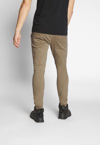 Brązowe spodnie o dopasowanym kroju, wykonane z miękkiego materiału, z talią o średnim stanie i czystym designem. Noszone z czarnymi butami sportowymi.