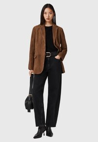 Bruine suède blazer, zwart gestructureerd sweater, zwarte high-waisted jeans, brede riem met gouden hardware, zwarte haklaarzen, schoudertas.