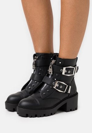 Czarne botki za kostkę wykonane z teksturowanej syntetycznej skóry, z metalowymi elementami w kolorze srebra, wieloma paskami, zamkami błyskawicznymi oraz grubą, żłobioną podeszwą.