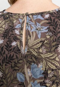Tecido estampado em tons castanhos com flores azuis e verdes, apresentando uma abertura em forma de tecla nas costas, fixada por um pequeno botão.