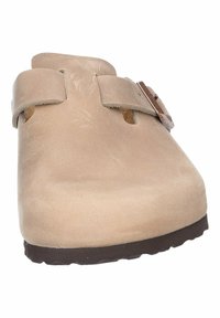 Beige mocka träskor med två justerbara remmar, en rund tå och en texturerad gummisula för grepp och komfort.