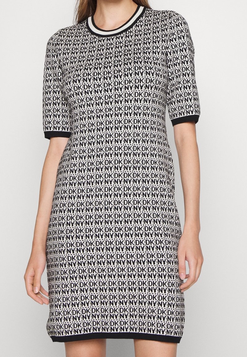 Femme portant une robe en maille noire et blanche à manches courtes avec un motif répété de logo "DKNY" et des bordures noires aux manches et à l'ourlet.