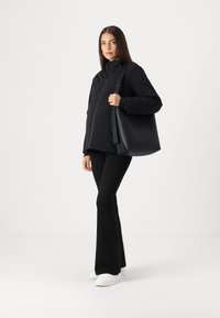 Black puffer jacket with high collar, paired with black flared pants and white sneakers. Model holds a large black tote bag.