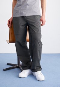 Dunkelgraue Hose mit lockerer Passform, aus strukturiertem Stoff und mit dezenten Nähdetails, kombiniert mit weißen Sneakers.