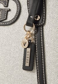 Grande borsa con materiale testurizzato bianco e nero, dotata di accessori in chiave dorata e di un'etichetta in pelle nera con la scritta "GUESS."