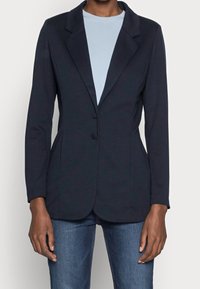 Námořnický blazer s dobře padnoucím designem, se špičatým límcem, dvěma knoflíky, bočními kapsami a hladkou texturou, navrstvený přes světle modrou košili.