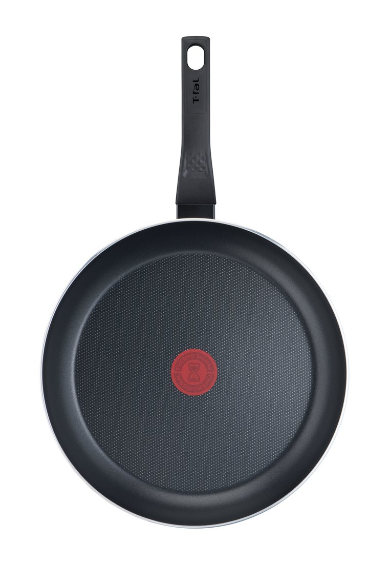 Poêle à frire antiadhésive avec une surface texturée noire, un indicateur de chaleur rouge au centre, et une poignée noire avec un trou pour suspendre.