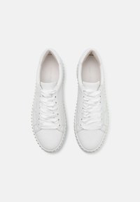 Weiße Leder-Sneaker mit flachen Schnürsenkeln, abgerundeter Zehenform, strukturiertem Sohle und runden Nieten entlang des Randes für zusätzliche Details. Glatte Oberfläche.