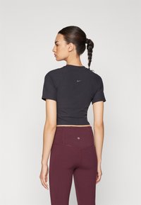Must have lühike varrukas must ülaosa soonikkangaga ja väike sinine Nike logo selja taga, koos kõrge vöökohaga burgundia värvi retuusidega.