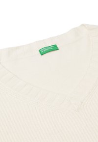 Cremfarbener Strickpullover mit V-Ausschnitt und Rippenstruktur am Kragen, ausgestattet mit einem grünen Etikett, auf dem "United Colors of Benetton" steht.