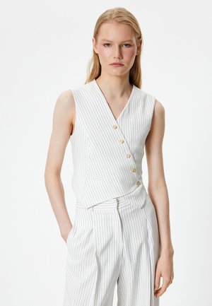 Haut sans manches blanc avec des rayures verticales, design en V, et boutons dorés ; présente une silhouette ajustée et des détails de couture en diagonale.