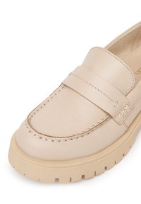 Bežové kožené mokasíny s prešívaným dizajnom a štvorcovou špičkou. Obsahujú široký remienok cez prednú časť a hrubú, textúrovanú podrážku.