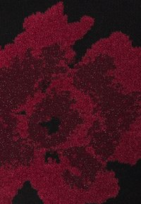 Motif floral rouge avec pétales texturés sur fond noir sur tissu tricoté, gros plan.