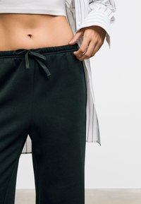 Zwarte sweatpants met een elastische tailleband en trekkoord, gecombineerd met een witte top en een lichtgestreepte button-up blouse. Gladde textuur.
