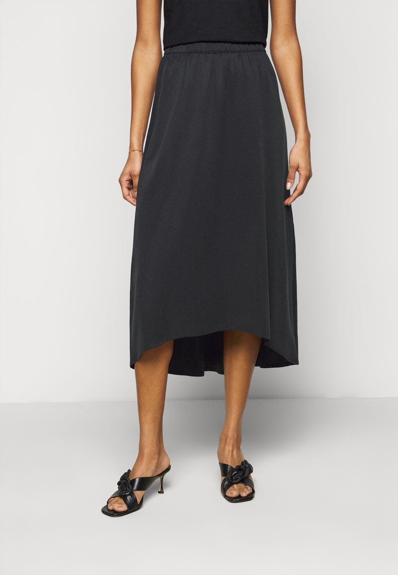 Black, mid-length skirt with an elastic waistband and a high-low hem. Accompanied by black heeled sandals with a bow accent.