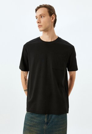 Sort kortærmet t-shirt med rund halsudskæring og en lommekant, lavet af blødt stof, parret med blå jeans.